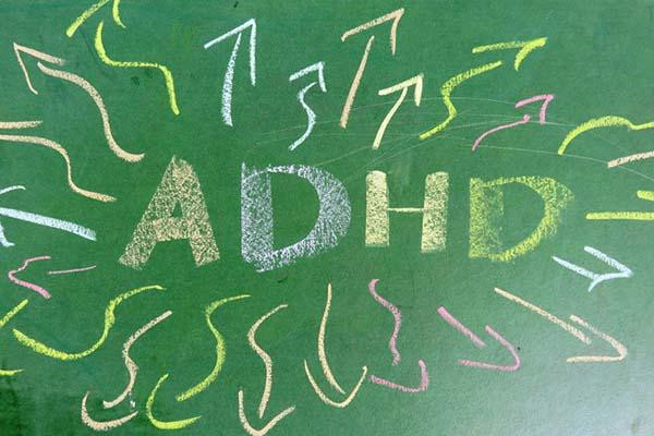 A green blackboard with the letters A D H D in chalk, with hand-drawn, squiggly arrows in multiple colors of chalk pointing outward in all directions from the letters.
